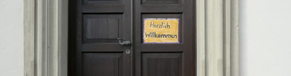 Kirchentüre aus Holz mit Willkommensschild. Elfriede Klauer in pfarrbriefservice.de